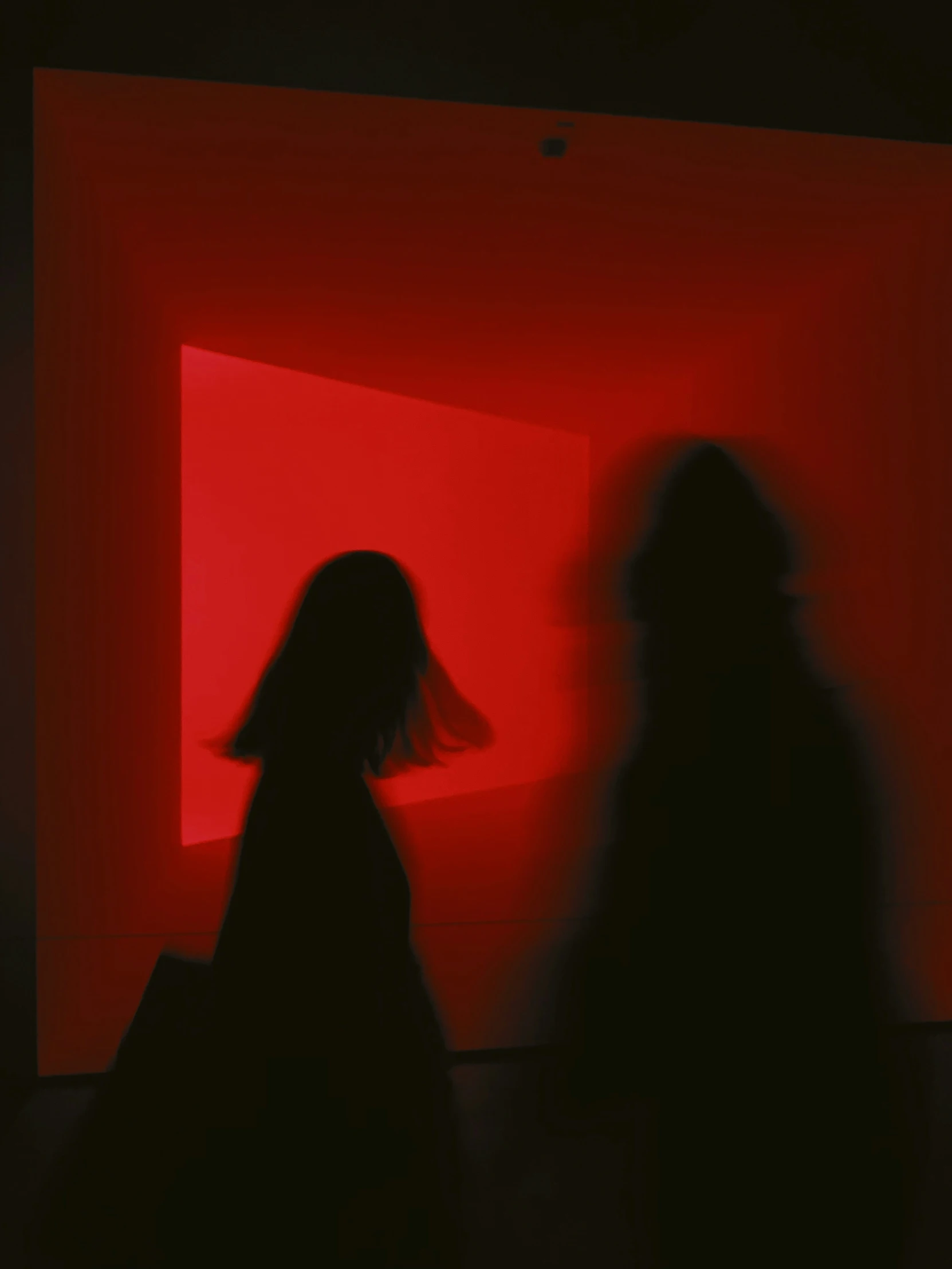 two women standing next to each other with dark red walls in the background