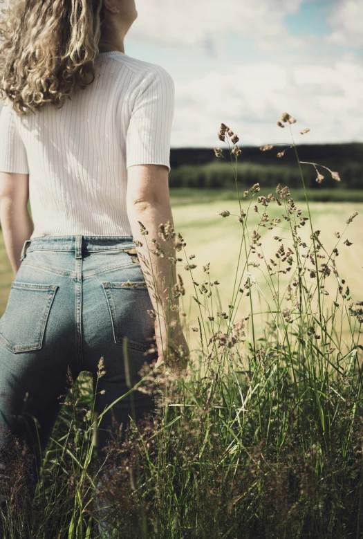 the back view of a woman standing in a field looking at tall grass