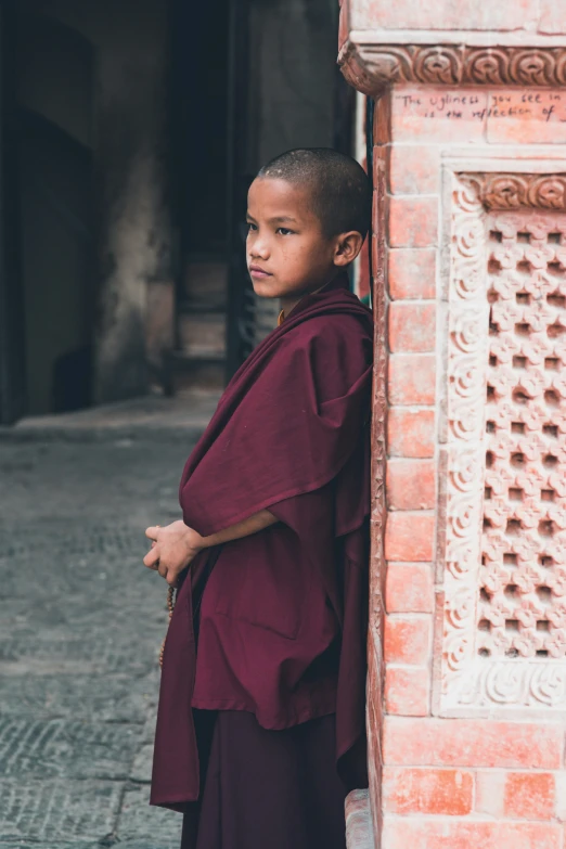 a boy in a monk outfit leaning against a building
