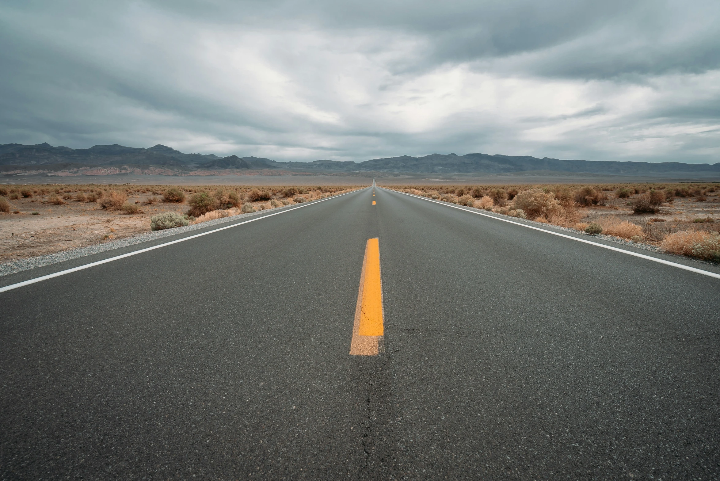 the asphalt road in the desert has two orange stripes