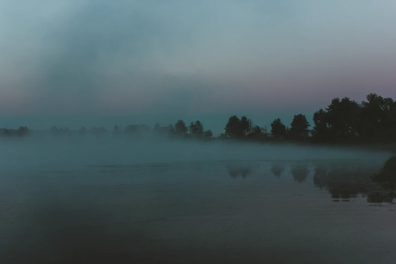 a body of water near trees in the fog