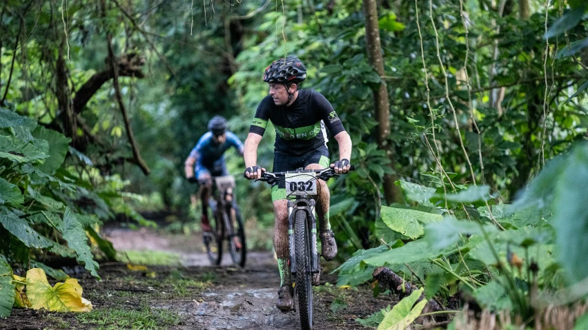 two people riding bikes on a trail through lush forest