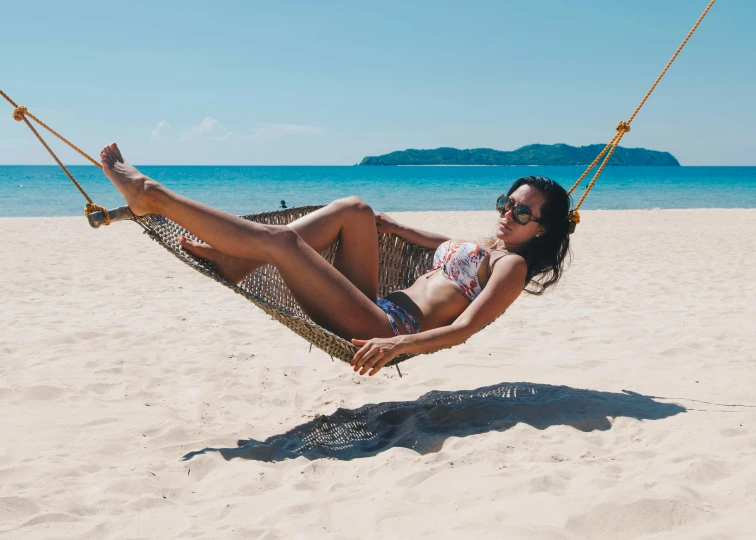 a beautiful young woman laying in a hammock on the beach