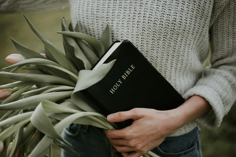 a person is holding up a book next to some green plants