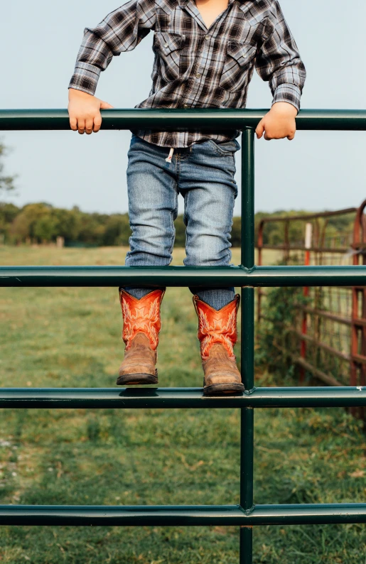 a little boy standing on top of a green gate