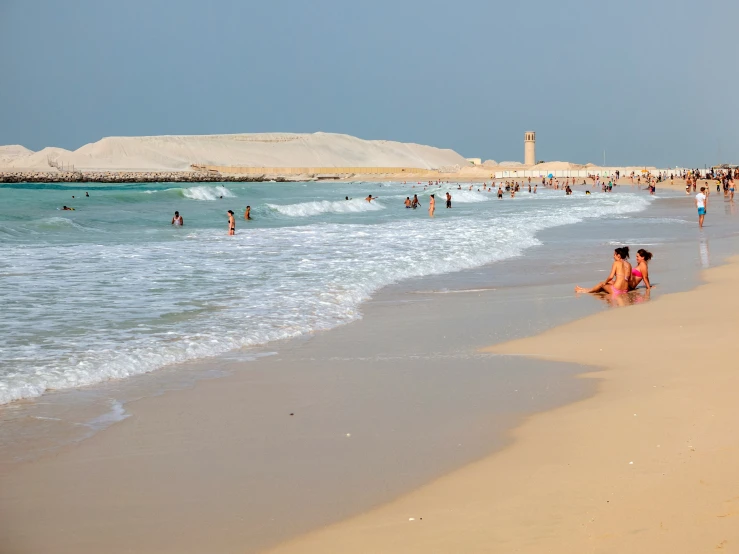 many people walking and swimming on a beach near the water