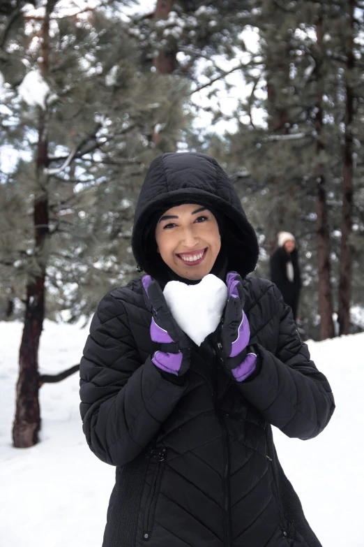 a woman is in the snow making a heart with her hands