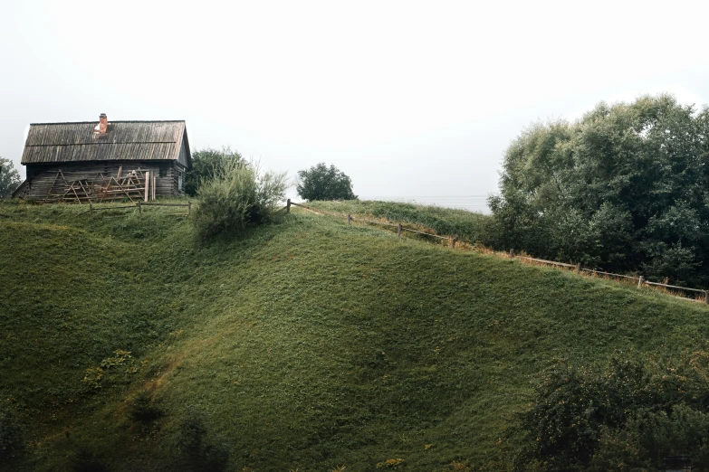 a small house on a grassy hill next to a forest