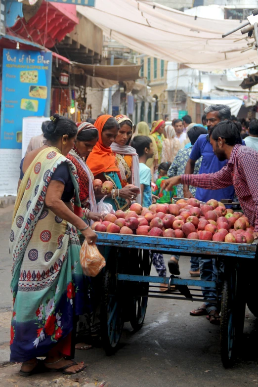 people standing around and sitting around a table that is full of fruits