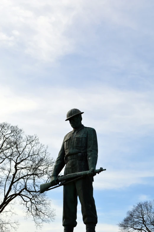 a statue of a soldier stands in front of trees and clouds