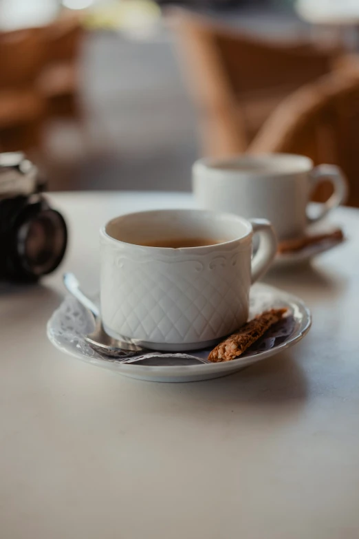 two coffee cups on a white table and another cup with a camera nearby