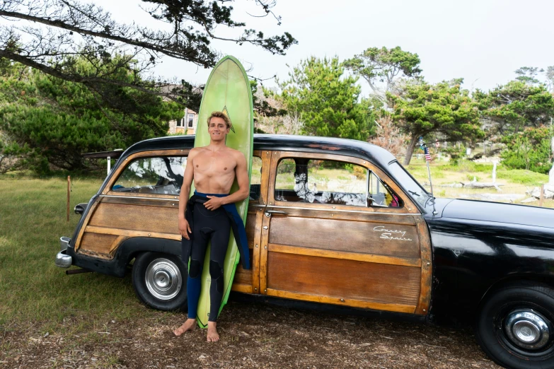 a man with a surfboard standing next to an old car