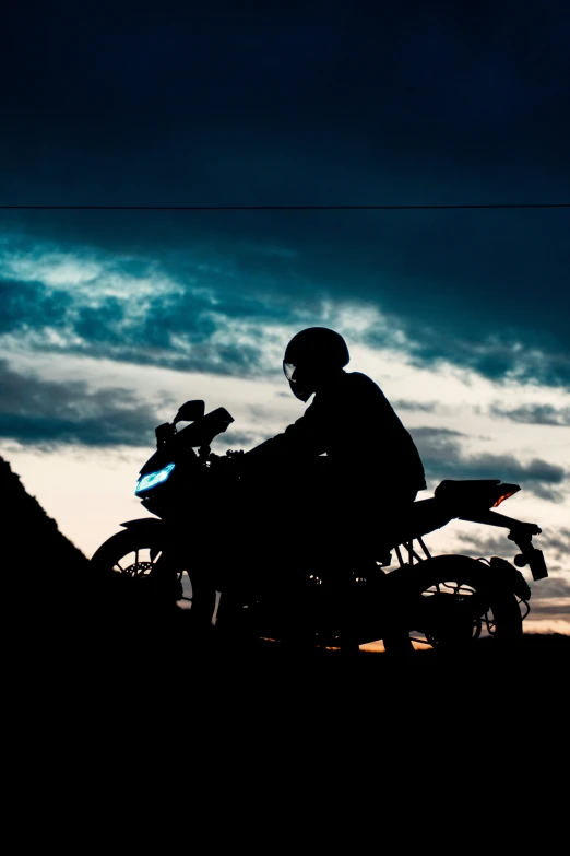 a silhouette of a man sitting on a motorcycle at sunset