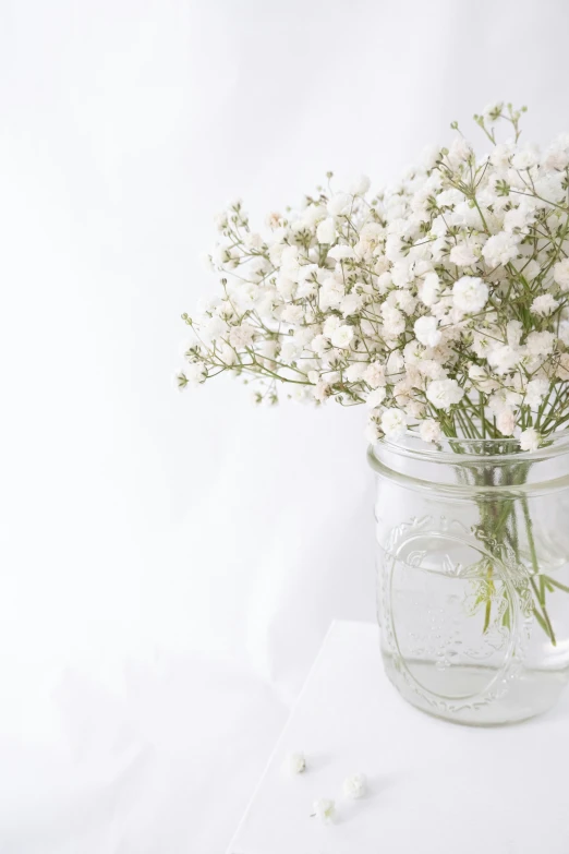 white flowers in a jar sitting on the table