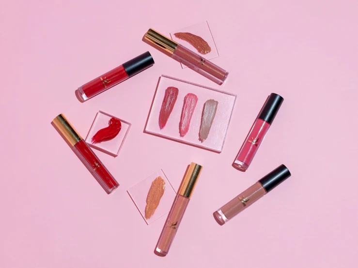 five different types of lip glosses on a pink surface