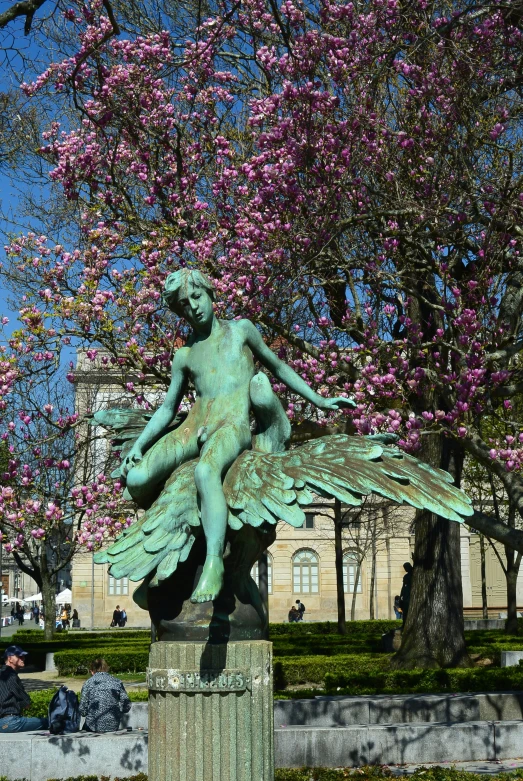 a green statue of an angel in front of some trees