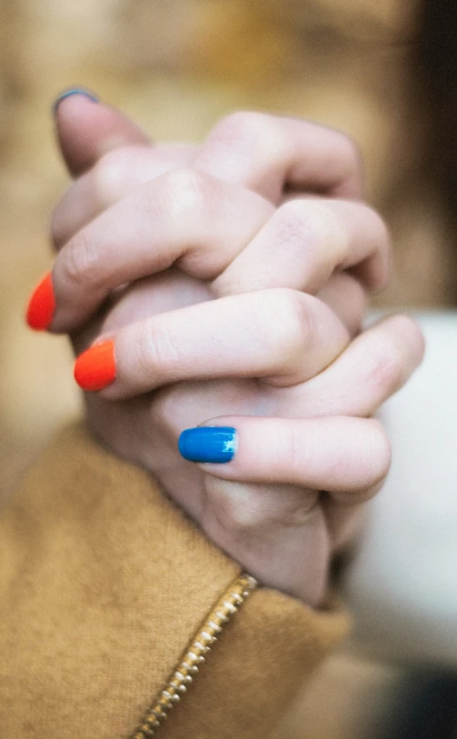 a close - up of two hands wearing bright colored nail polishes