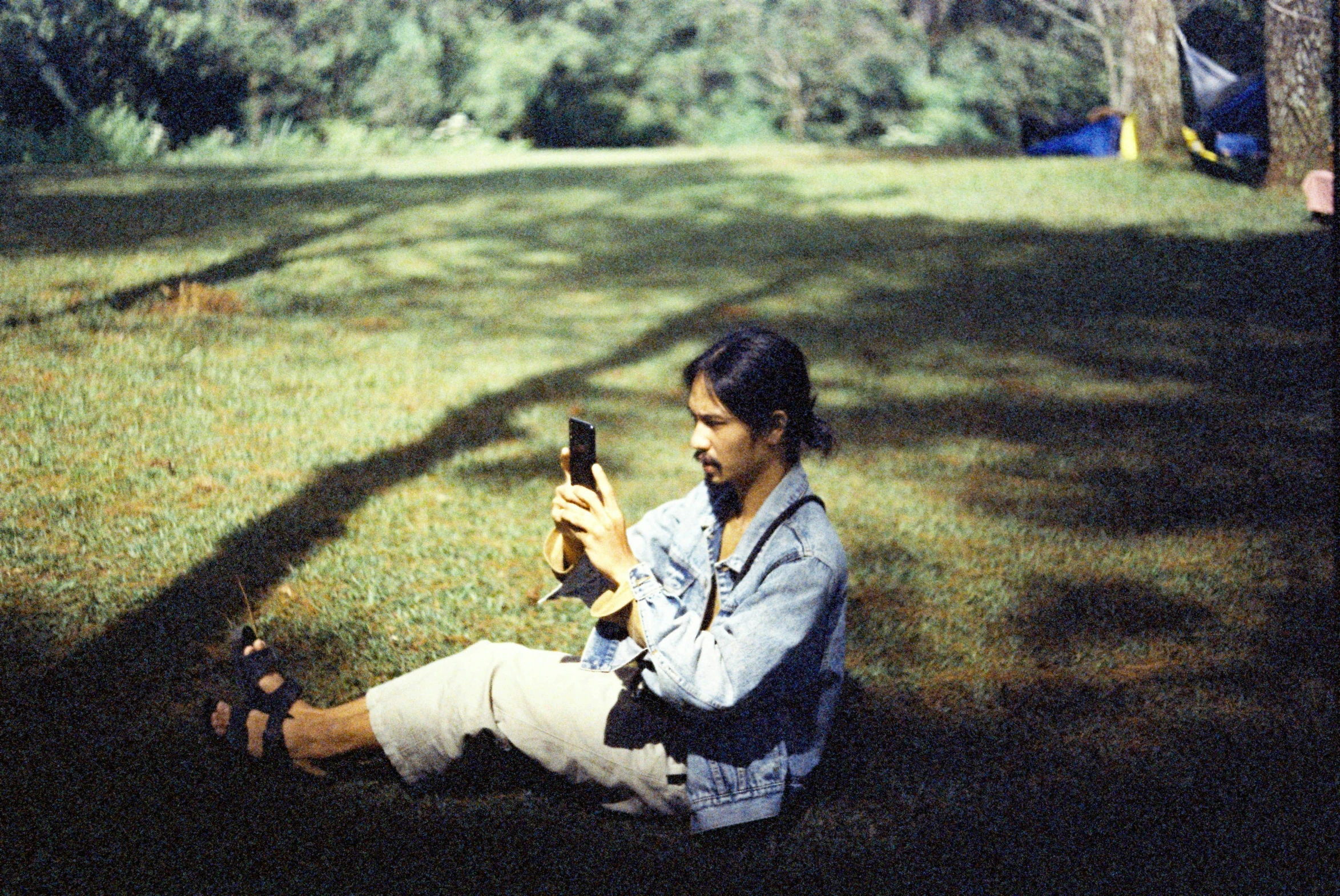 a man sits in the shade looking at his phone