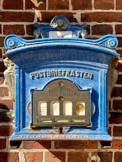 a blue postbox on a brick wall with the word postmaster