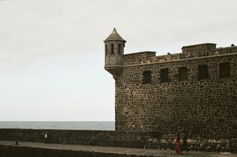 a stone tower and a brick wall by the ocean