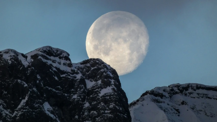 a clear sky, with a large moon visible in the sky over some snowy mountain tops