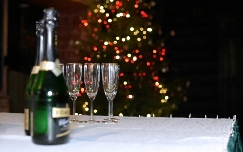 three wine glasses with champagne are lined up in front of a lighted christmas tree