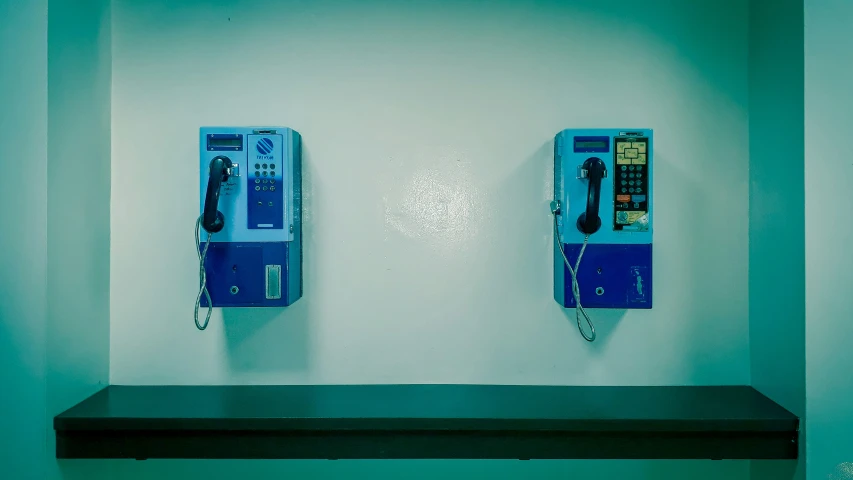 two phones hanging up on the wall by a shelf