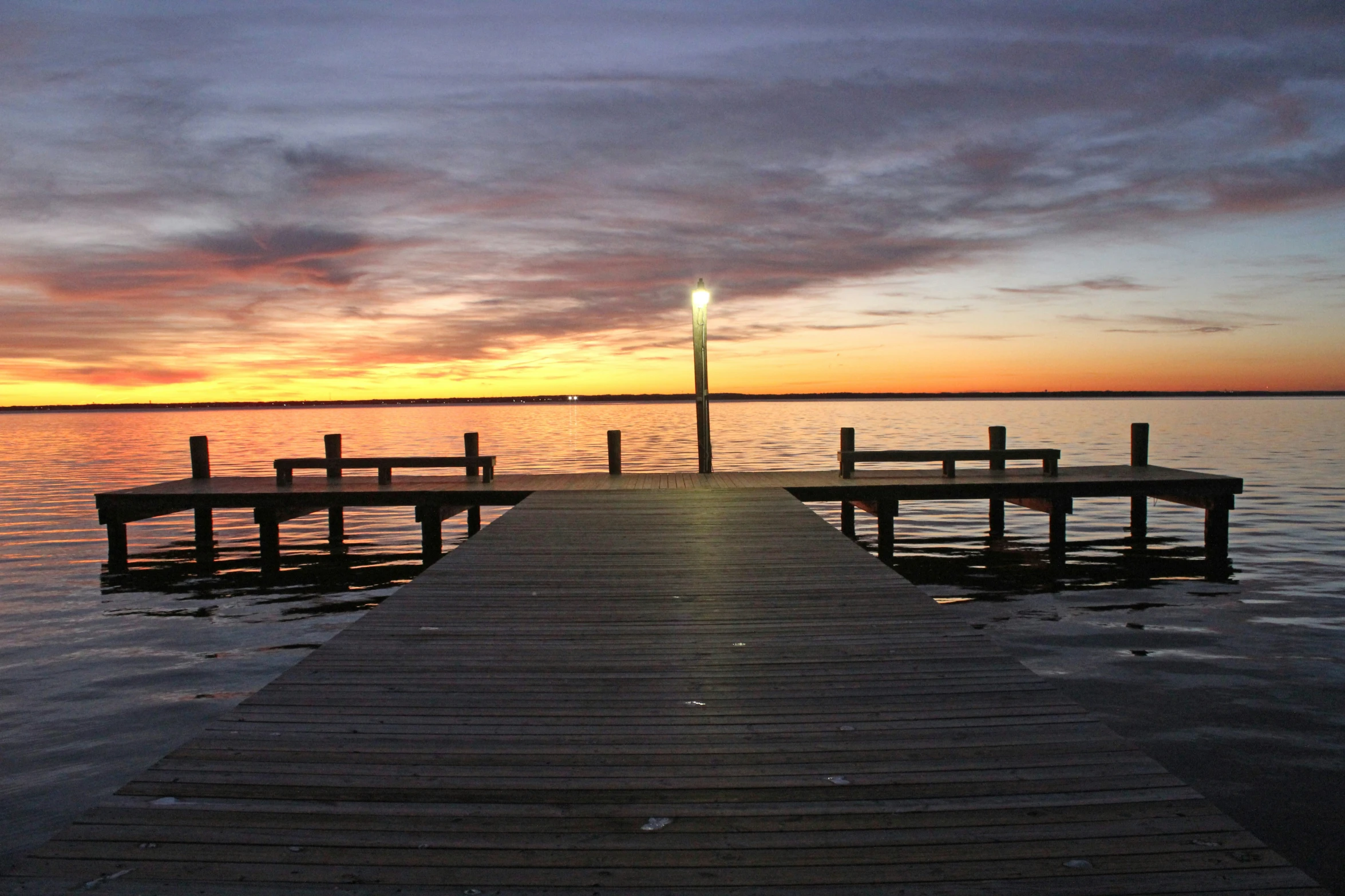 the pier has three benches on it at sunset