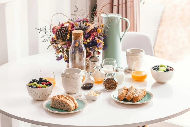 a small dining table with coffee, juice and a plate of bread and fruit