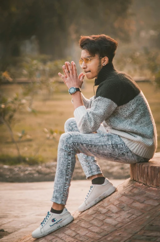 an asian male sitting on brick wall posing