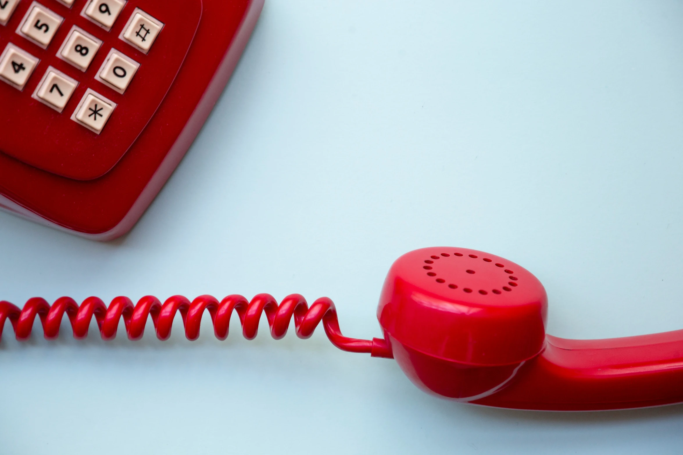 a red phone on a white table with two old telephones next to it