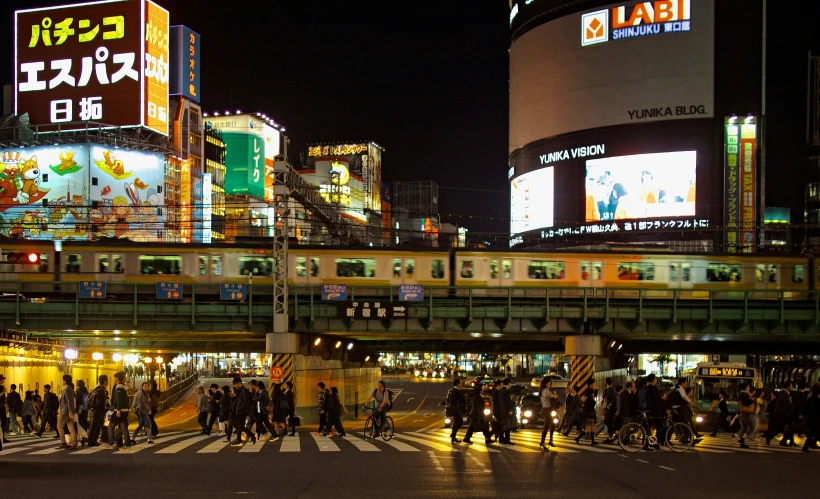 pedestrians crossing a city street at night with advertits lit up