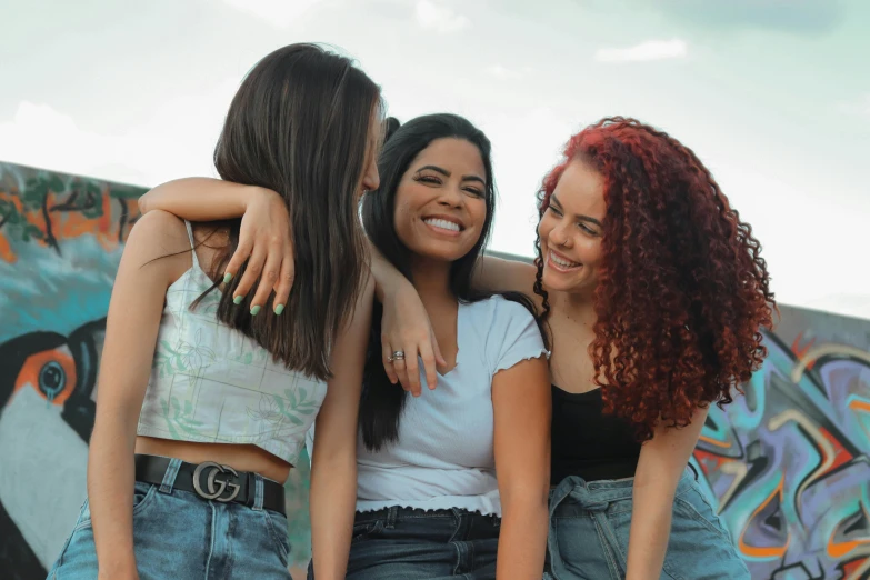 three smiling young women are hugging and looking at the camera