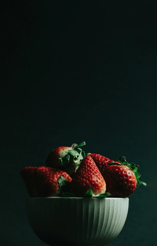 a bowl of strawberries on a dark green background