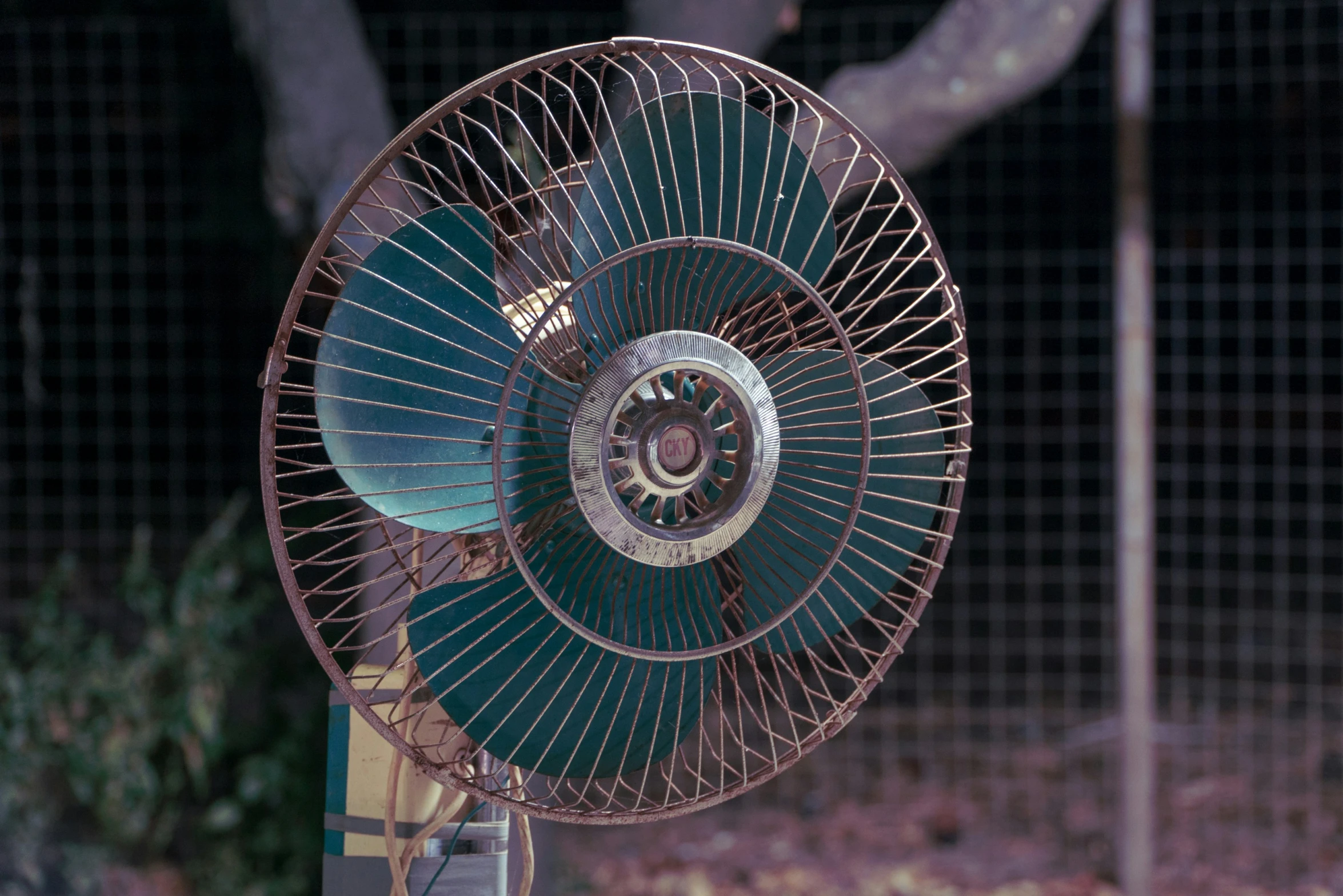an old electric fan hanging in front of a chain link fence