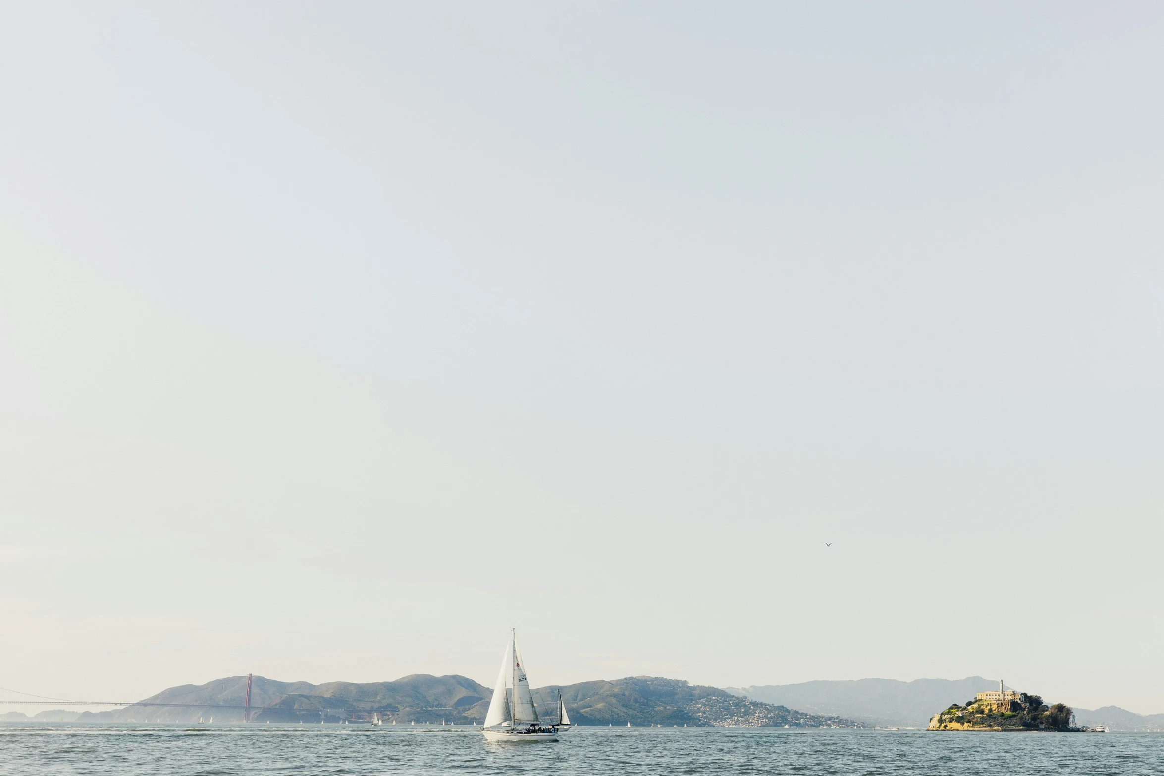 sailboat on open ocean near island in front of sky