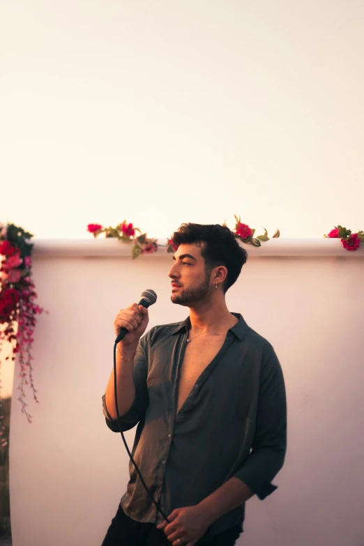 man holding microphone standing on roof above flowered plant