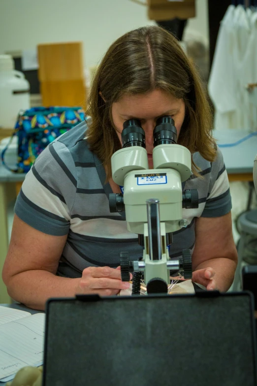 the woman looks through her binoculars in front of the laptop