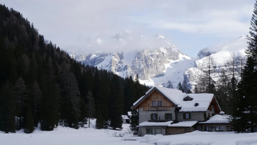 a house with snow on it standing in the middle of a mountain