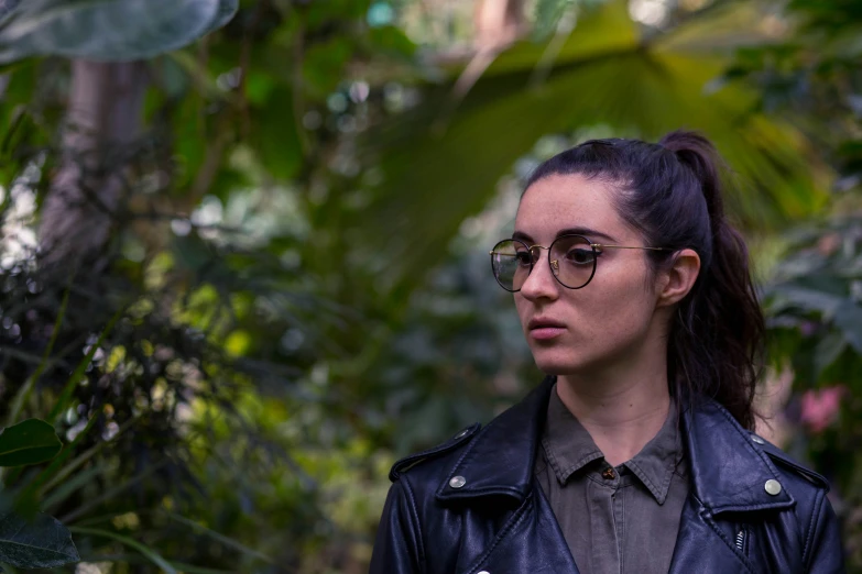 a woman in glasses stands under many leaves