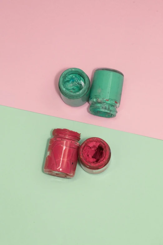 two bottles of paint next to one another on a light blue, green and pink background