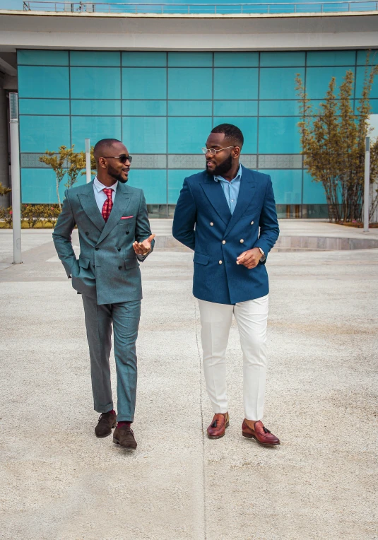 two men in blue suits are standing on a sidewalk