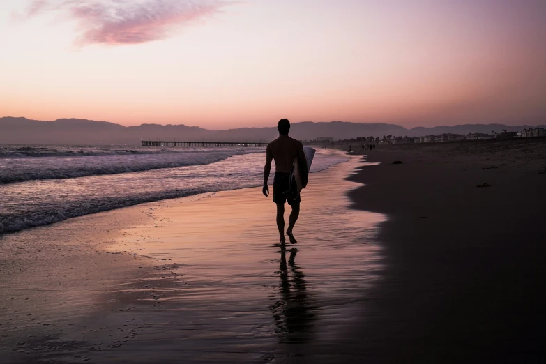 a man holding onto the edge of a surfboard walking along the beach