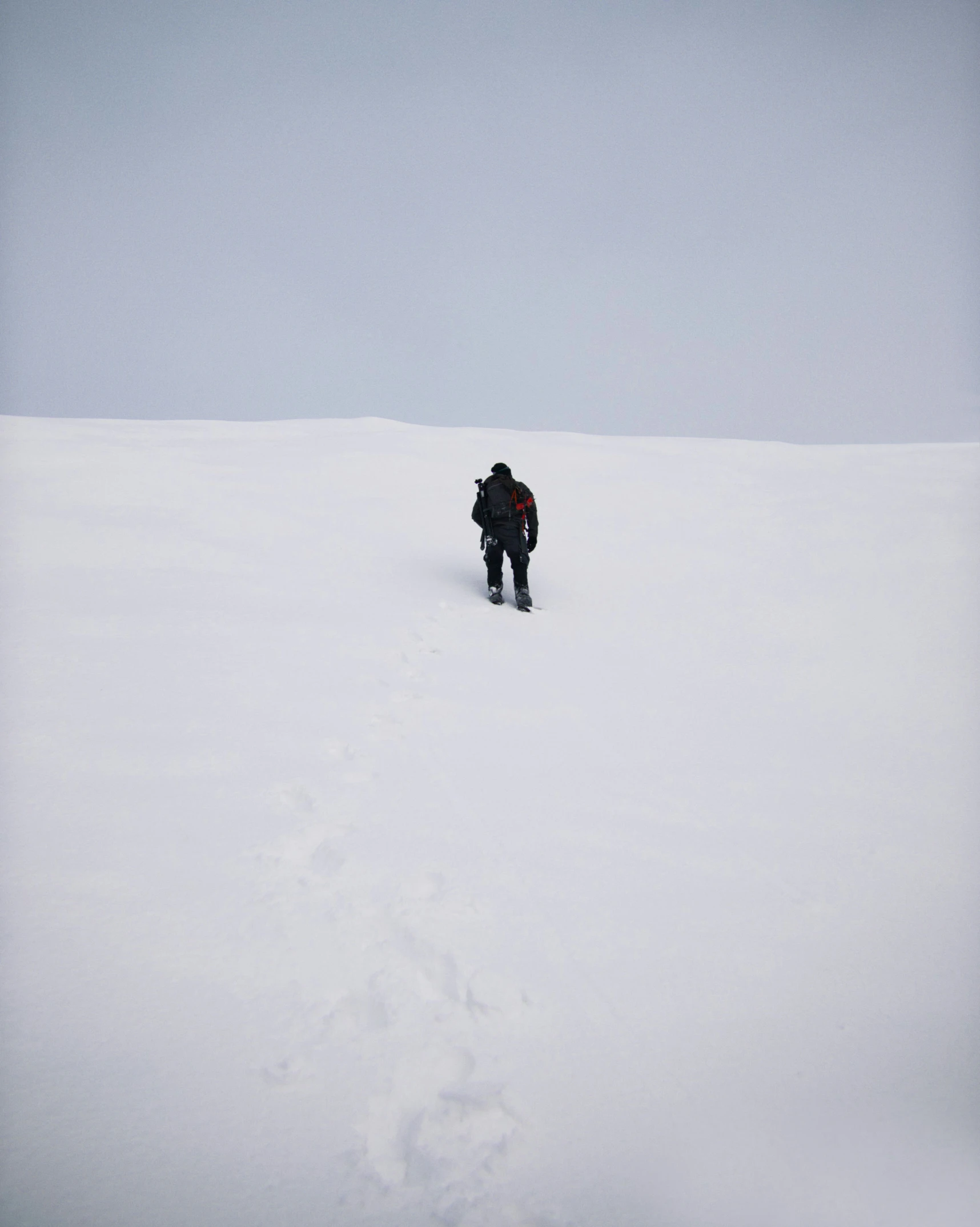 the lone person in black stands on the snowy hill