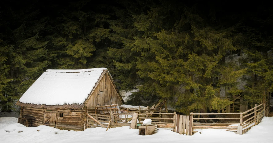 an old barn stands in the snow surrounded by trees