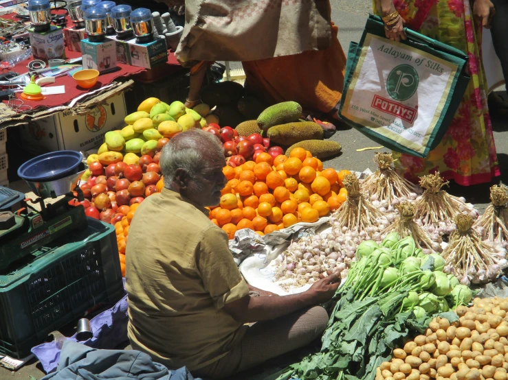 an old man is seated in front of fruit and vegetables