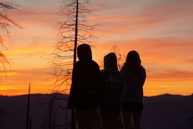 three people standing looking down at the sunset