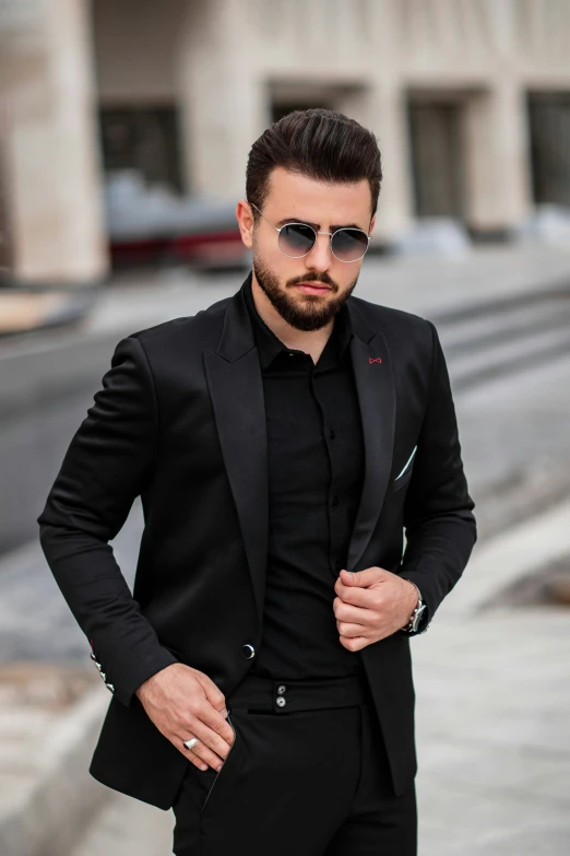 a man in a black suit and shades poses on a city street
