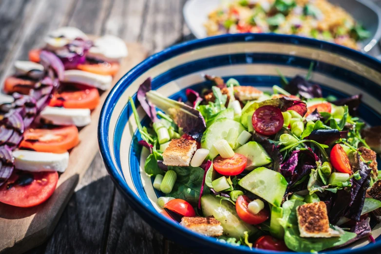 a blue bowl of salad with cucumber, tomato slices and other vegetables