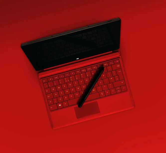 a laptop on a red surface with a red pen